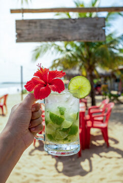 Hand holding caipirinha cocktail on a tropical brazilian beach