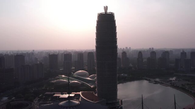 A silhouetted tall skyscraper stands by a lake in a sprawling modern urban cityscape at dusk.