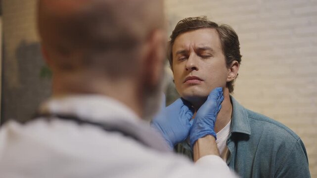 ENT doctor palpates male patient's neck during consultation and medical check-up