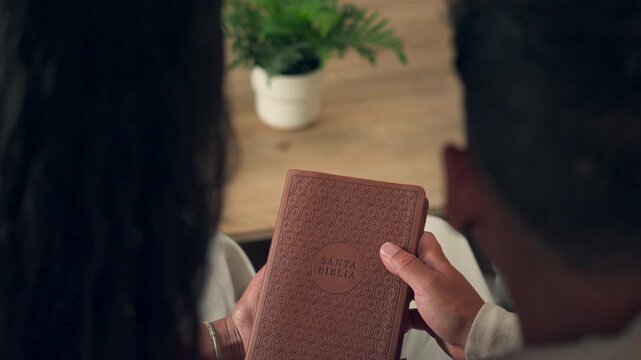 Close up of a young couple looking at a closed Spanish Holy Bible at home