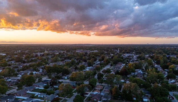 Aerial view of the residential neighborhood of Trenton at sunset, featuring rows of houses, lush green trees, and a dramatic sky in Trenton, Michigan, United States.