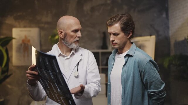 Orthopedist shows male patient X-ray scan and explains diagnosis during check-up