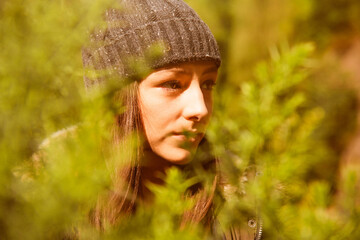 Woman in nature wearing knit hat, surrounded by greenery