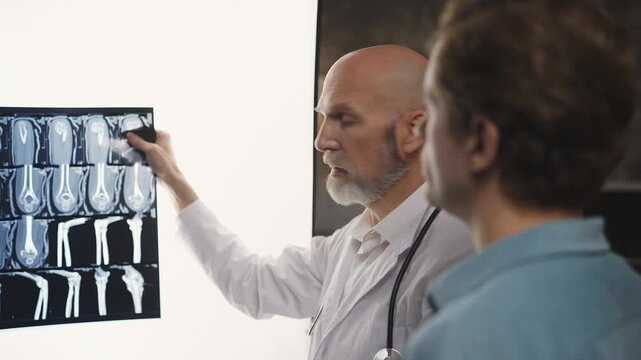 Orthopedic surgeon reviews limb injury X-ray with male patient during check-up