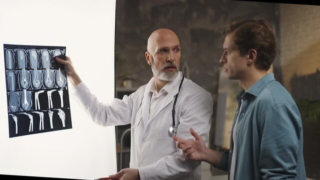 Orthopedist explains bone X-ray results to male patient during health check-up