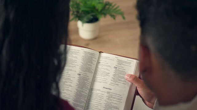 Young couple reading the Bible together from behind at home