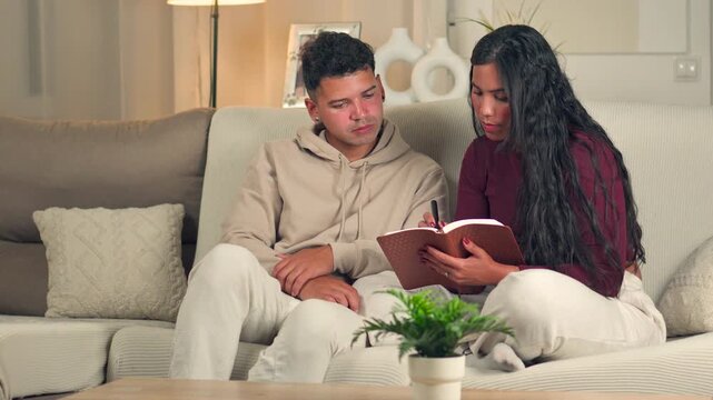 Young couple studying and highlighting verses in the Bible together on a sofa
