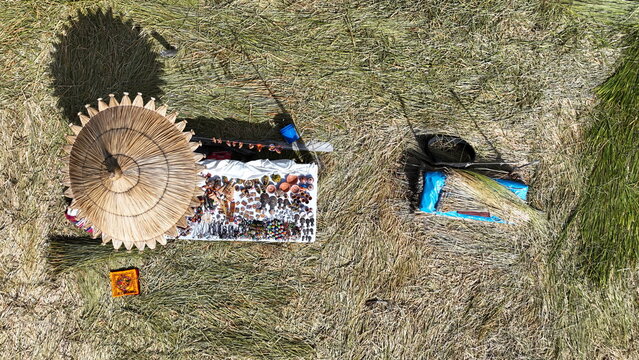 Aerial view of a traditional straw umbrella shading a display of handmade handicrafts on the floating reed islands of Lake Titicaca in Uros, Peru.