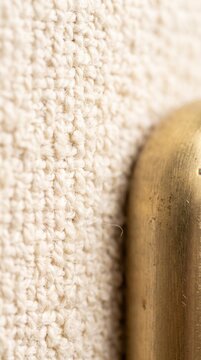 Vertical macro texture of woven cream boucl&eacute; fabric beside a rounded brass furniture leg