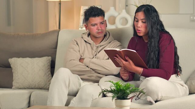 Wife reading the Bible aloud to her husband on a sofa at home