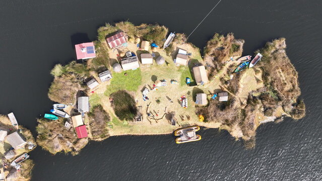 Aerial view of the Uros floating islands on Lake Titicaca, featuring traditional reed houses, small boats moored along the edges, and clear water. Urus, Peru.