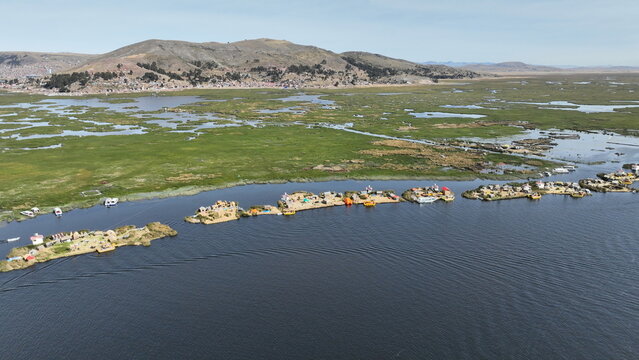 Aerial view of the Uros floating islands made of totora reeds on Lake Titicaca, surrounded by vast blue water and lush green wetlands under a clear sky in Urus, Peru.