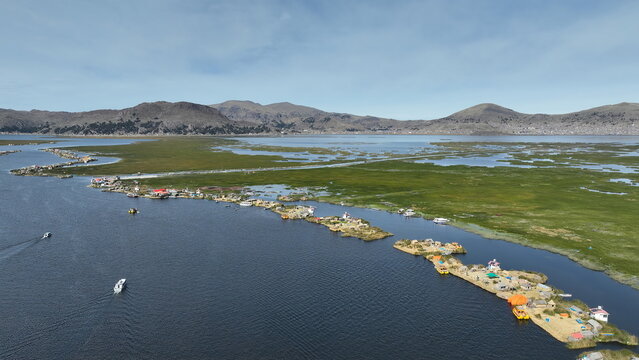Aerial view of the floating islands of the Uros people on Lake Titicaca with small boats navigating the blue water and distant mountains in the background, Urus, Peru.