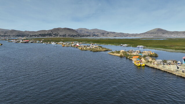 Aerial view of Lake Titicaca featuring Uros floating islands made of totora reeds, with traditional reed boats moored alongside, set against distant mountains Urus, Peru.