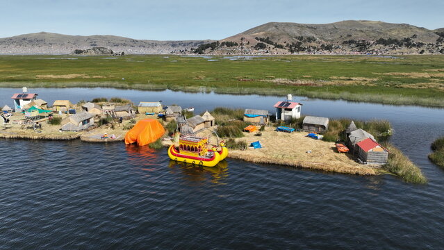 Aerial view of Lake Titicaca featuring the traditional floating reed islands of the Uros people with small huts and a bright yellow boat docked at the shore in Urus, Peru.