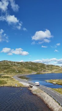 Aerial video of a road crossing remote mountainous terrain in Norway, surrounded by lakes, rocky landscapes, open countryside and dramatic Nordic scenery beneath a blue sky, 4k.