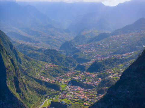 Aerial view of the Curral das Freiras valley nestled between steep green mountains with small houses and terraced fields in Curral das Freiras, Madeira, Portugal.