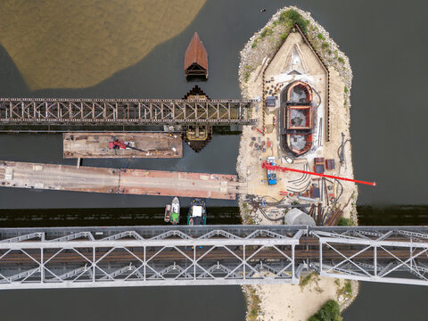 Aerial view of the bridge construction site on the Vistula River featuring steel trusses, heavy machinery, and a crane on a sandbank in Tczew, Poland.