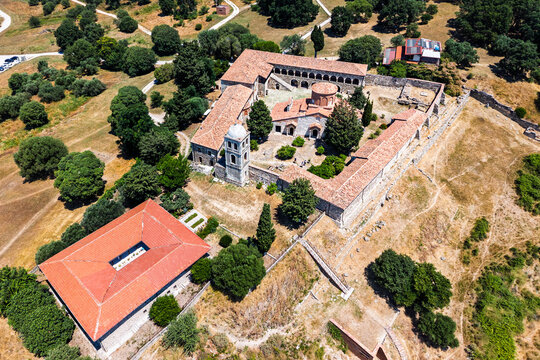 FIER, ALBANIA. Apollonia Archaeological Park. Aerial drone view of a historic monastery complex with red tiled roofs, stone ruins, trees and dry Mediterranean landscape.