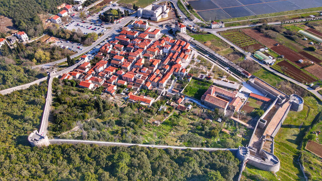 Aerial view of the historic town of Ston with its iconic medieval defensive walls, red-tiled rooftops, and surrounding lush greenery in Ston, Dubrovnik-Neretva County, Croatia.