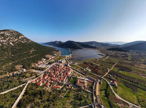 Aerial view of the historic town of Ston and its ancient defensive walls, surrounded by salt pans, lush green hills, and the Adriatic coastline in Ston, Dubrovnik-Neretva County, Croatia.