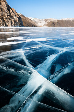 Blue transparent cracked ice and rocks on Baikal lake, Siberia, Russia.