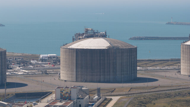 Aerial view of the Dunkirk LNG Terminal featuring a large cylindrical storage tank within an industrial facility near the coast in Loon-Plage, Hauts-de-France, France.
