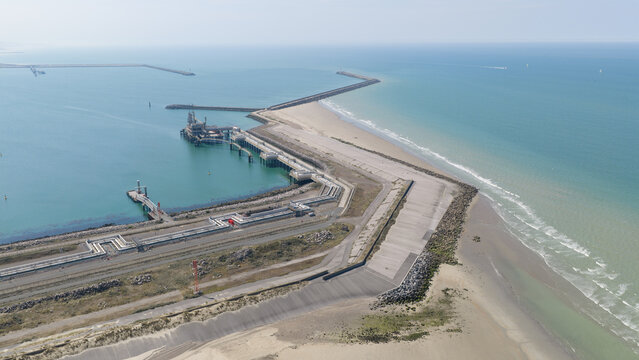 Aerial view of Dunkirk LNG Terminal with its industrial infrastructure, jetty, and storage tanks situated along the sandy coastline and the North Sea in Loon-Plage, Hauts-de-France, France.