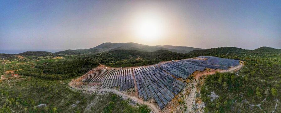 Aerial view of the solar farm on the island of Vis, with rows of photovoltaic panels set against rolling hills and Mediterranean vegetation under a golden sunset in Split-Dalmatia County, Croatia.