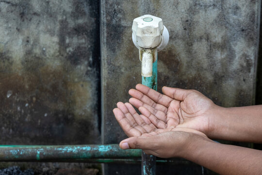 Cupped hands waiting for drop under dirty plastic water tap against concrete wall. Powerful visual for water crisis, climate change, and hygiene issues.