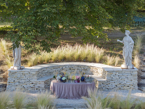Aerial view of a stone bench flanked by classical statues in a garden setting with a table decorated with flowers in Vallery, Bourgogne-Franche-Comte, France.