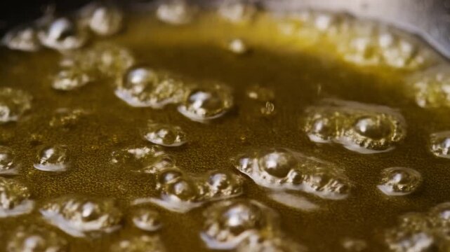 Slow motion close up of bubbling golden caramelizing liquid simmering in pan on stovetop in kitchen