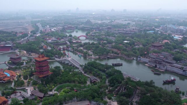 Aerial panorama of a traditional scenic area with waterways, ancient architecture, and greenery under hazy sky.