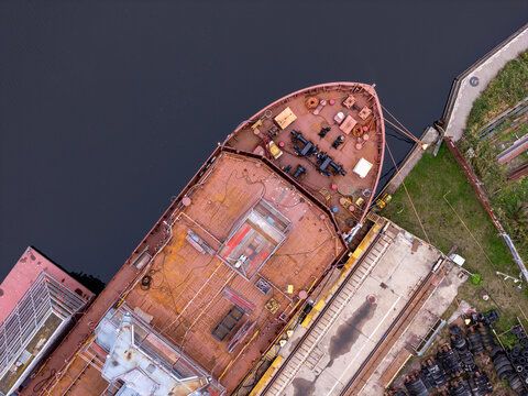 Aerial view of the bow of a large cargo ship docked at an industrial shipyard with rusty deck surfaces and nearby concrete quays in Gdansk, Poland.