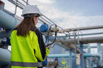 Fototapeta premium Female engineer inspecting water treatment pipelines with a digital tablet at a water supply plant. Concept of infrastructure, utility maintenance, water management and safety.