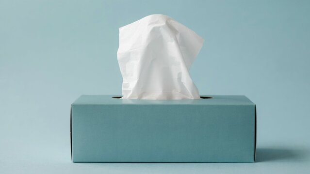 White facial tissue pulling out of a blue cardboard box on a light blue background