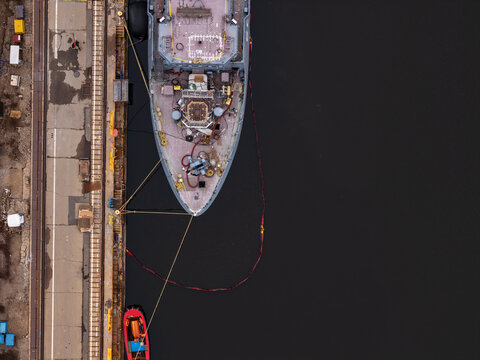 Aerial view of a military ship docked at a shipyard pier with mooring lines and industrial infrastructure in Gdansk, Poland.
