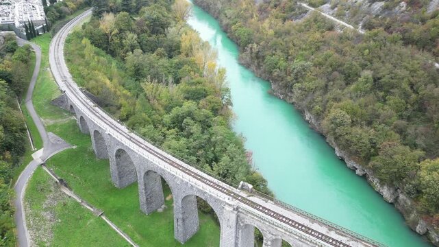 Aerial perspective of the historic Solkan Bridge, a stone arch railway viaduct crossing the emerald green Soca River in Slovenia