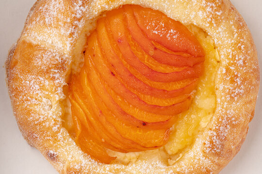 Fresh baked danish pastry bun filled with sliced apricot custard cream and dusted with powdered sugar close up
