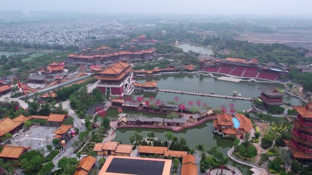 An aerial shot of a traditional Chinese garden complex with lakes, historic architecture and lush greenery, set in an urban area.