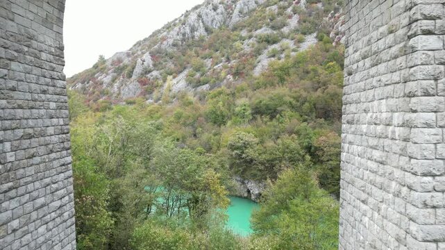 Aerial shot revealing the emerald Soca River from behind the historic stone arches of the Solkan Bridge, a famous landmark in Slovenia