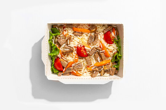 Traditional oriental pilaf with beef meat rice carrots and cherry tomatoes in takeaway paper box on white