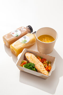 Healthy meal delivery set with baked salmon fillet roasted vegetables creamy soup and juice bottles on white