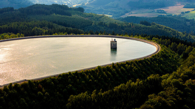 Aerial view of a pumped storage power plant reservoir surrounded by dense green forests and rolling hills in Germany.