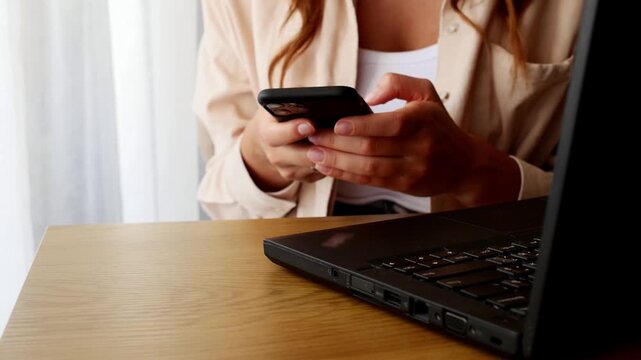 Close up woman texting on smartphone beside laptop, online communication and remote work