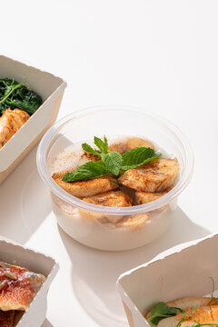 Healthy dessert porridge topped with sliced bananas ground cinnamon and fresh mint in plastic takeaway cup