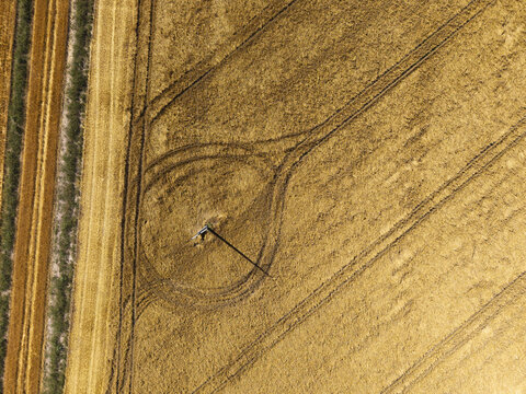 Aerial view of a golden wheat field with intricate tractor tire tracks forming circular patterns around a central pole in Poland.