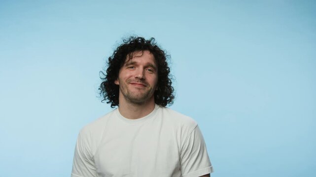 Portrait of young Caucasian man turning to face camera and laughing on blue background. Footage is perfect for promoting mental wellbeing apps or dental hygiene services