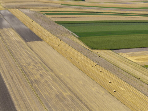 Aerial view of harvested wheat fields with scattered hay bales and diverse agricultural plots in Poland.