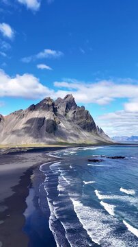Aerial video of Stokksnes beach in Iceland, featuring dramatic black volcanic sand, rugged coastal formations and mountain scenery along the Atlantic shoreline, 4k.